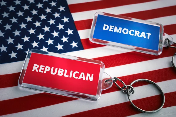 the keychain of the Republican Party and the Democratic Party on the background of the US flag. Opposition of Republicans and Democrats concept. Elections in the United States of America.