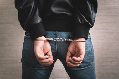 Elleri arkadan kelepçeli tutuklu bir adam. Mahkum kavramı, hapisteki bir mahkumun elleri kelepçeli, erkek mahkumlar karanlık cezaevinde ağır şekilde zorlandı, şiddet, kelepçeli eller...