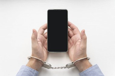 Tahta beyaz masadaki yakın çekimde kelepçe ve cep telefonu. Tutuklandığında veya gözaltına alındığında arama hakkı