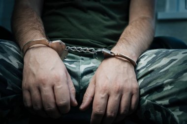 Askeri asker kelepçeli, elleri arkada, karanlık bir geçmişi var. Kavram: Savaş suçlusu, savaş esiri, mahkeme. Sorgulanan bir savaş esiri..