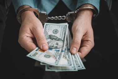 Elleri kelepçeli ve arka planda ABD doları var. Paraya bağımlılık kavramı. Finans dünyasında suç. Suçlu iş adamı, rüşvetçi memur, vergi kaçıran