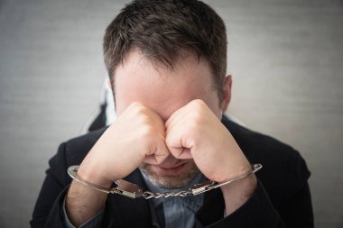 a sad man is crying in handcuffs. A corrupt official in the police for questioning. The guy in the jacket hides his eyes during the arrest. clipart