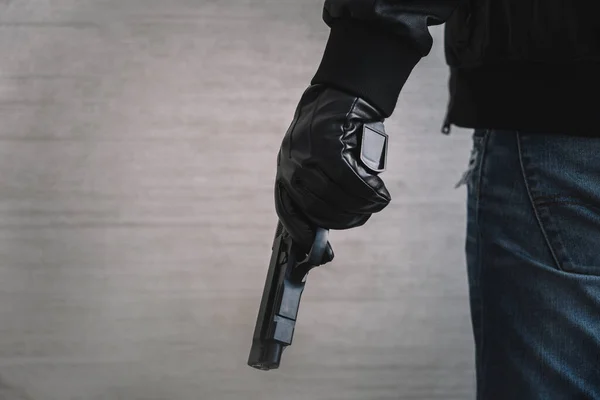 stock image The concept of the crime of banditry. A dangerous shooter and a black pistol on a dark background. The hired killer is preparing to shoot. Pulls a firearm out of his jacket pocket