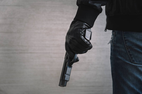 The concept of the crime of banditry. A dangerous shooter and a black pistol on a dark background. The hired killer is preparing to shoot. Pulls a firearm out of his jacket pocket