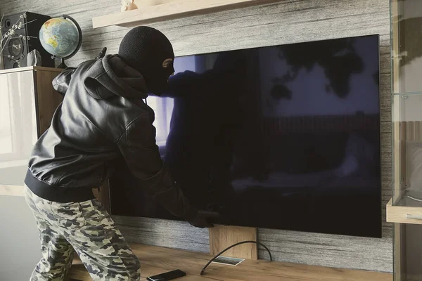 マスク泥棒は壁から高価なテレビを削除します アパートの盗難の概念 選択的焦点 — ストック写真