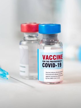 İki şişe Cavid 19 Coronavirus aşısı ve beyaz masada bir şırınga. Covid-19 salgınıyla mücadelenin tıbbi konsepti. dikey resim