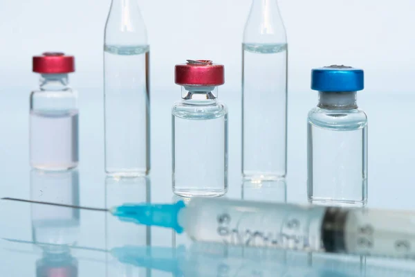 stock image glass vial of liquid, a vaccine, and a medical syringe close-up on a blue background. The concept of vaccination against coronavirus . Banner, copy space.