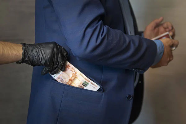 A hand pulls paper money out of his jacket pocket. A thief robbed a businessman. Cash theft, criminal concept.