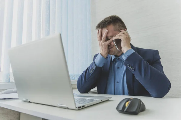 stock image Tired or exhausted man closing his face with hands sitting in front of computer in office. businessman covers his face and eyes with his hands. facepalm man talking on the phone