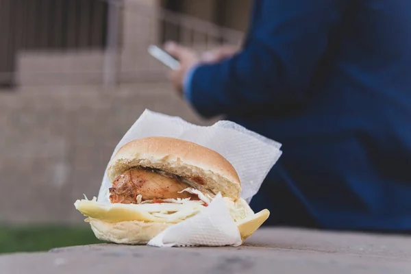 chicken sandwich lying on a bench on the street. The concept of junk food on the lunch break. Businessman eats unhealthy high-calorie food on the street against the background of an office building
