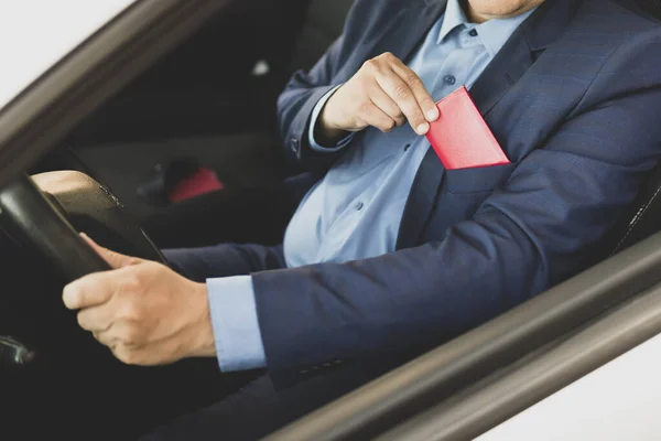 A rich businessman in a blue suit shows a red pass or document sitting in an expensive car. The politician holds an identity card in his hand. blank document for text and design. copy space