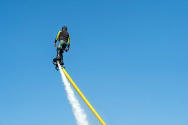 Mavi gökyüzünün arka planında bir adam Flyboard 'da uçuyor. Sıra dışı spor