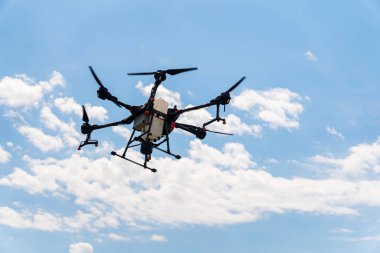 Bir püskürtücü dron bulutlarla mavi gökyüzünde buğday tarlasının üzerinde uçuyor. Akıllı çiftçilik ve hassas tarım. Gökyüzünde endüstriyel bir dron.