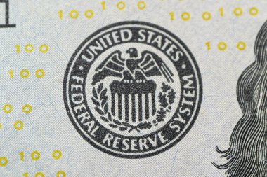 Federal Rezerv Sistemi logosu yakın plan. FED faiz artışı, ekonomi ve enflasyon denetimi ulusal organizasyonunu düşünürken, ABD Merkez Bankası 100 dolarlık banknota amblem koydu.