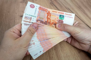 Mavi arka planda genç bir iş adamının elinde çok para var. Beş bin ruble değerinde bir yığın Rus rublesi. Başarılı iş adamı