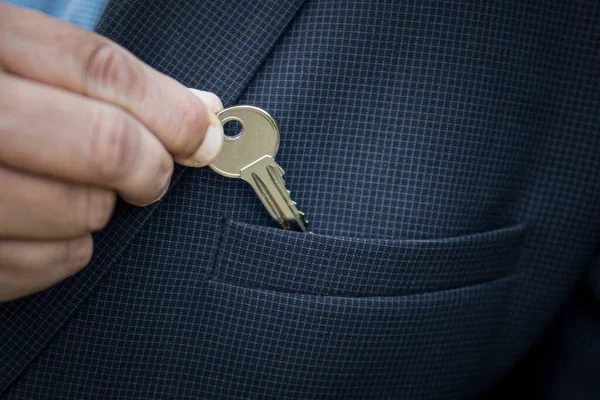 a businessman puts a small key to a safe deposit box or a bank in his jacket pocket the concept of saving money. The real estate agent takes out the key to the apartment.