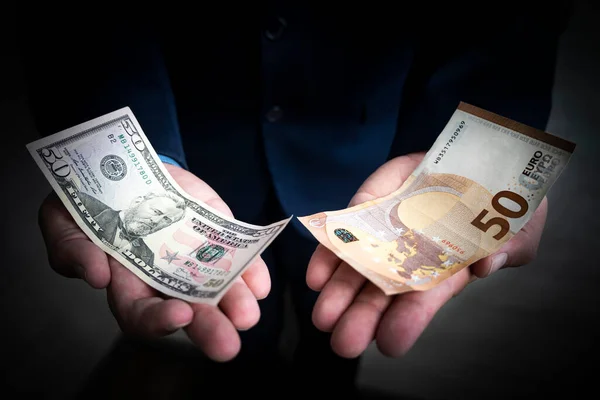 the concept of choosing between the dollar and the euro. Banknotes of 50 euros and fifty dollars in the hands of a businessman on a dark background. Equality of exchange rates.
