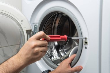 Young plumber fixing washing machine in bathroom, closeup clipart