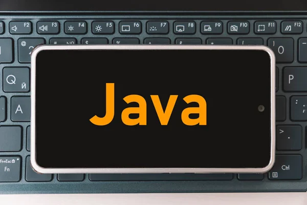 Java Programming language for mobile development, concept. Smartphone on the laptop keyboard, the programmer workplace. inscription java on the mobile phone screen ,