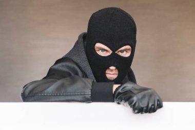Maskeli kötü bir hırsız beyaz bir tahtanın arkasından dışarı bakar. Yüzünde maske olan kötü bir haydut..