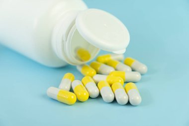 Mavi masadaki beyaz plastik bir kavanozdan saçılan sarı haplar. Sağlık tıbbı ve eczane kavramı. İlaç üretimi.