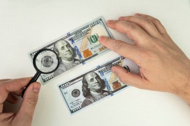 Kalpazan sahte banknotlar hazırlar. Sahte konsept. Sahte Amerikan doları, büyüteç. Parayı büyüteç altında görmek. filigran, su izi. Sahte banknotlar için arama