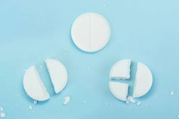 White pills on blue background. Few pills broken in half, reducing the dose of the medicine. round tablet was divided equally