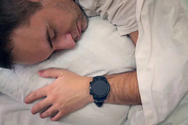 heartbeat monitoring with a smart gadget in a dream. man sleeps on a white pillow with a smartwatch on his wrist to monitor his heartbeat. a blank screen on the clock. blank smartwatch screen