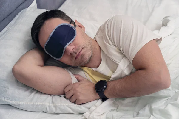 Young Man Sleeping On Bed Using blue Eye Mask. A mask for sleeping on the eyes of a sleeper during the day soaring