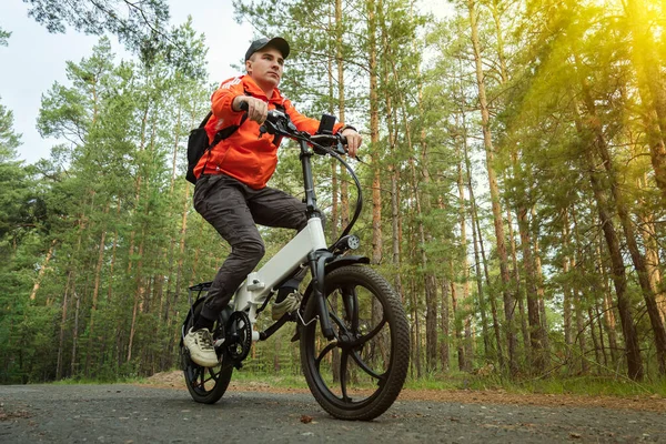 Spor konsepti. Bisikletçi tek pistte gidiyor. Elektrikli, modern bir bisiklete binmek. Alaşımlı tekerlekleri olan havalı bir bisiklet. Bir bisikletçi yeşil ağaçların arka planına doğru gidiyor.