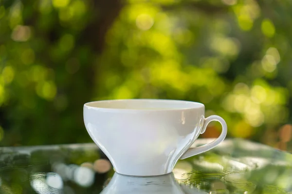 White coffee cup or mug on natural stone table against blurred green background of fresh summer greenery. Coffee time calm, peaceful, rural way of life oudoor. Empty space for text or design