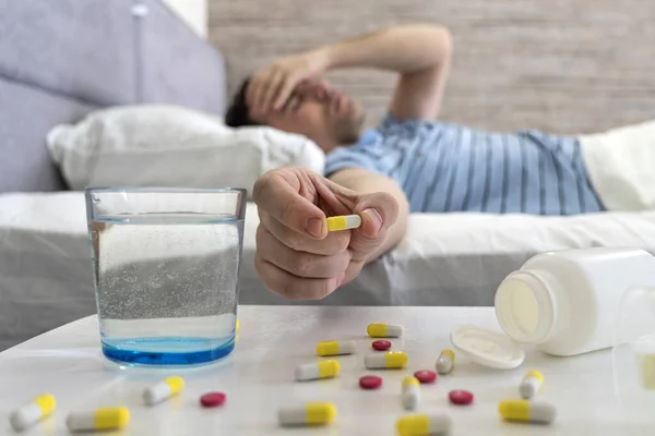 young man taking medicine pill for hangover in bed at home, suffering from headache, migraine. a man suffers from a headache during a cold while lying on a bed in the bedroom