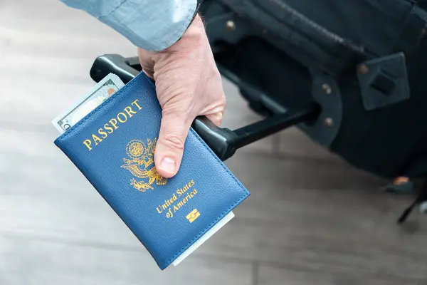 a man\'s hand with an American passport and luggage in close-up. The concept of migration and travel. Foreign trips. Flights in the United States of America