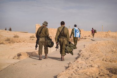 İsrail ordusunun bir kaç askerinin İsrail bayrağıyla yürüdüğünü gösteren bir fotoğraf. Askerler diğer askerlerle yürüyor. Savaş taktik tatbikatı. Piyadeler yerlerinden çekiliyor.