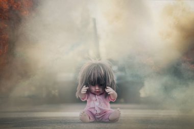 Korkmuş bir bebek ateş ve dumanla çevrili yerde oturuyor. Saldırı tankının arka planında bir çocuk oyuncağı. Askeri çatışmaların dehşeti kavramı. Savaş ve çocuk kavramı.