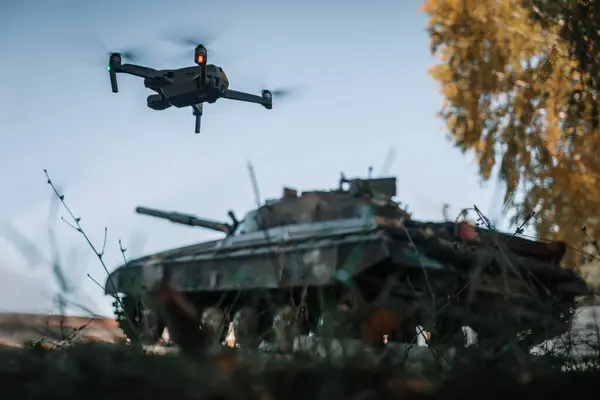 a drone flying above the tank in the background in nature. help of reconnaissance drones in modern warfare.