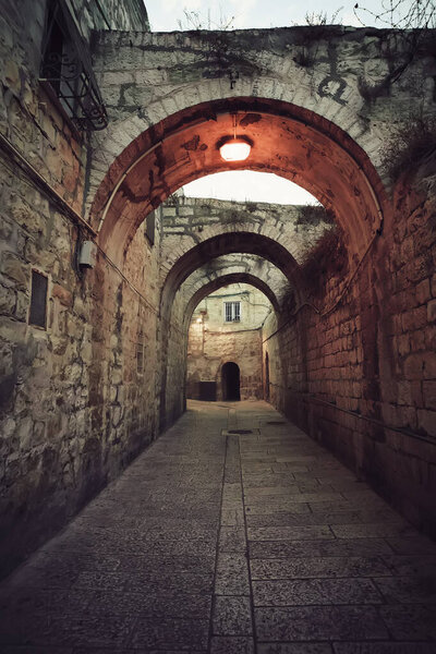 Ancient deserted alley in Jewish Quarter in the Old City Jerusalem with switched on street light on the vault. Old narrow street with archeway construction. Empty road of old quarter in early morning
