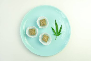CBD yağlı tatlılar. Kenevir yapraklı renkli şeker. Mavi arka planda marihuana yaprağı. Rahatlamak için yiyeceğin içindeki uyuşturucu maddesi. Üst manzara, düz uzanma.