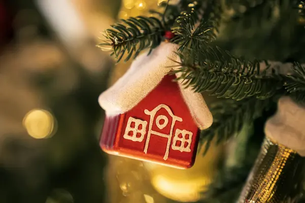Christmas tree toy in form of a house on a branch. Christmas mood background. Vacation atmosphere. Chousing rental concept, realtor services, mortgage, purchase, loan. Mortgage buying real estate