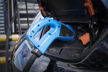 Elektrikli araba, şehir caddesinde elektrikli araba şarj istasyonuyla park yerinde şarj oluyor. Şarj edilen bir elektrikli arabaya mavi renk takılı güç kaynağını kapat.