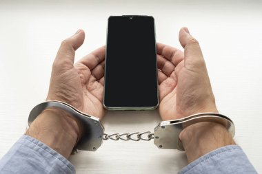 Kelepçeli adamın elleri ve cep telefonu. Bağımlılık kavramı. Akıllı telefonla kelepçelenmiş bir telefon dolandırıcısı..