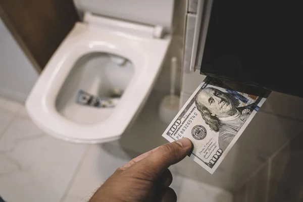 Flush money down toilet, throws dollar bills in the toilet, loss concept, close up, selective focus. concept of senseless waste of money, loss, useless waste, large water costs,