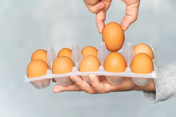 man checks the eggs in the box. a customer in a supermarket touches chicken eggs in a cardboard box. buying groceries in store. product selection on blue background