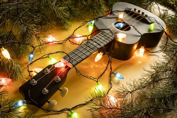 Koyu arkaplanda ışıklı çelenk olan ukulele gitar. Noel veya yeni yıl için hediye gitar klasik şekilleri.