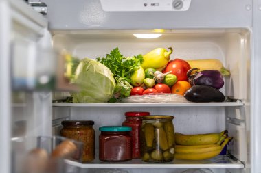 Modern buzdolabında bir sürü farklı taze ürün var. Buzdolabının rafında taze sebzeler var..