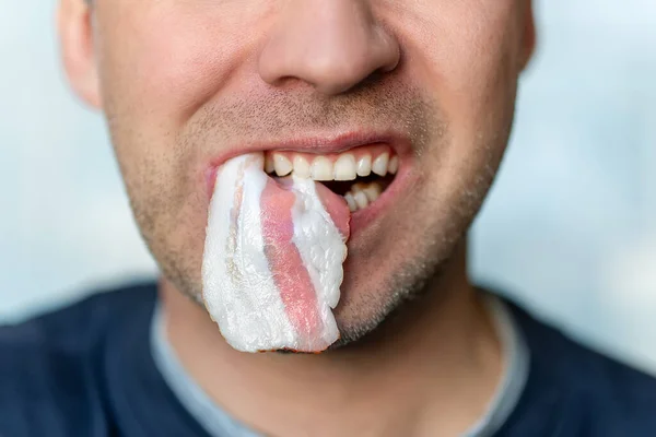 fat bacon in a male mouth in close-up. A man eats unhealthy fatty food.