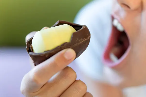 A baby girl bites a chocolate egg with a plastic toy inside. harmful dangerous food for children
