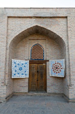 Özbekistan, Semerkand 'daki hediyelik eşya dükkanının girişinin önündeki duvarda küçük halılar asılı..