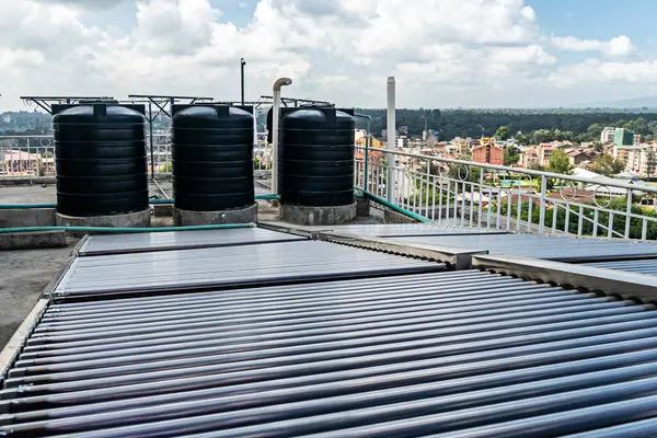 Water tank on the roof over blue sky. Black water tank on the roof of a tall building against a blue sky. a water heating system on the roof of a high-rise building in southern countries.