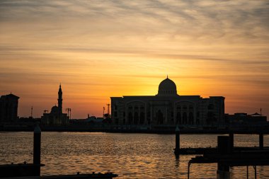Sharjah 'ta denizde güzel bir gün doğumu. Arap mimarisinin güzel binaları akşam güneşinin arka planında